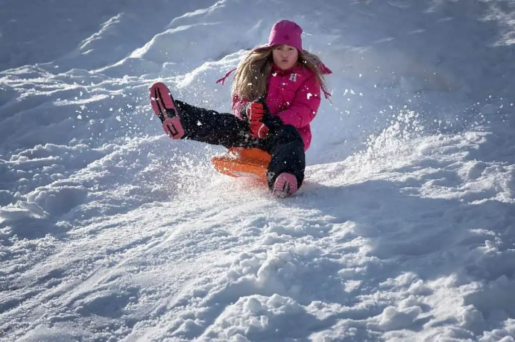 A girl speeding down a snowy hill on her toboggan in Banff. 