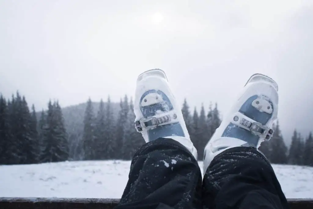 The legs of a skier in ski boots with a mountain in the background