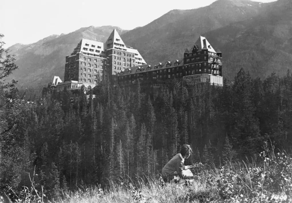 The center tower of the Banff Springs Hotel, with in the foreground a woman picking wildflowers