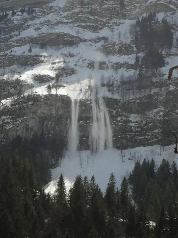 A stream of snow comes down a steep mountain cliff