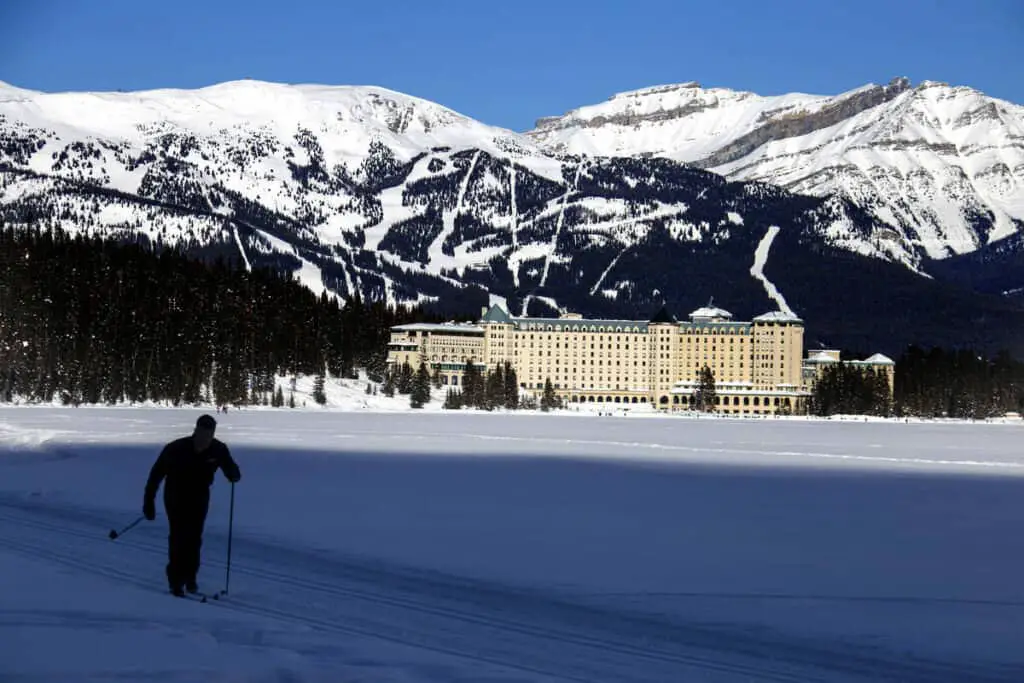 A frozen Lake Louise with the Château Lake Louise in the background and a cross-country skier in the foreground