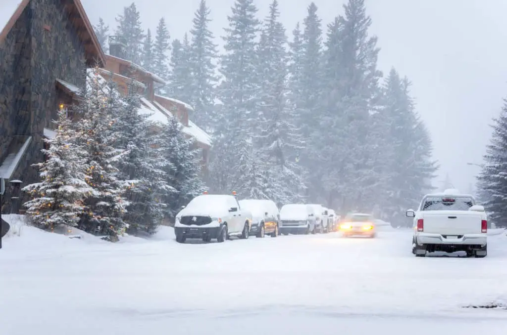Heavy snow ravages the town of Banff in a street with several parked vehicles at dawn in March