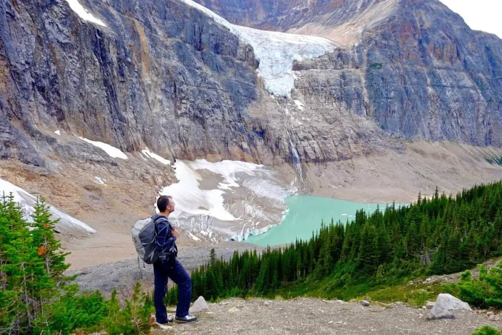A hiker is standing on a rock near a lake just below the Crowfoot Glacier in Banff National Park