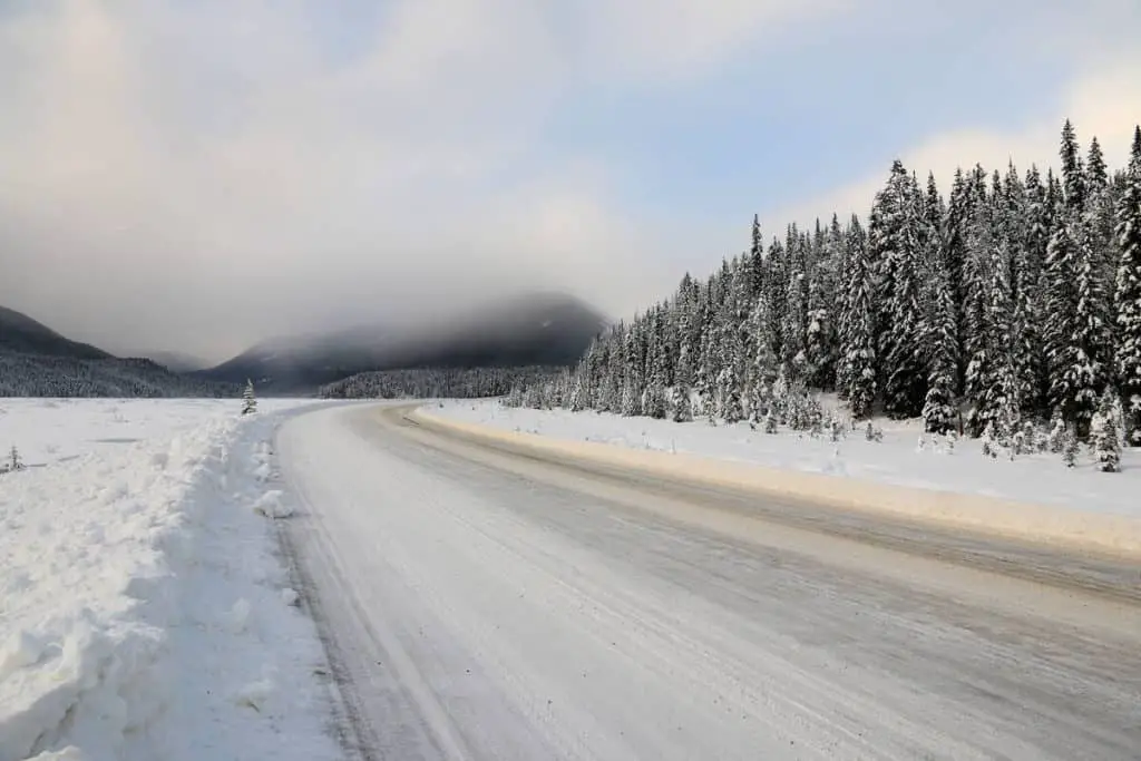 A snow-covered and icy road bordered by snow-covered pine trees in Banff National Park