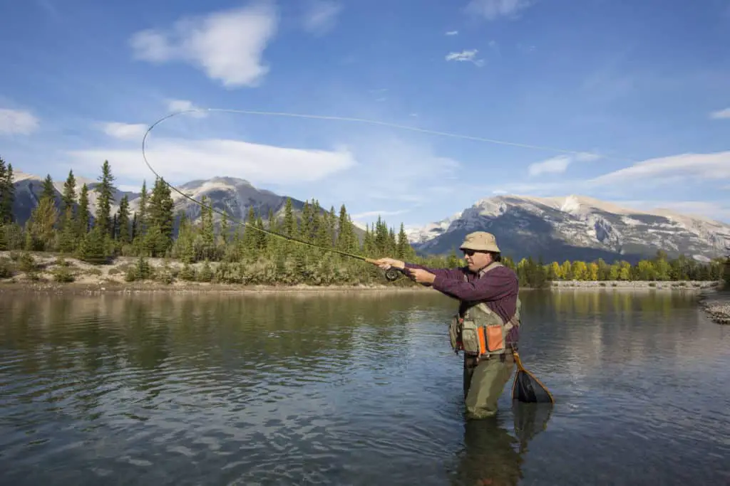 Man fly fishing while standing in the fast flowing Bow River with the Rocky Mountains of Banff National Park in the background
