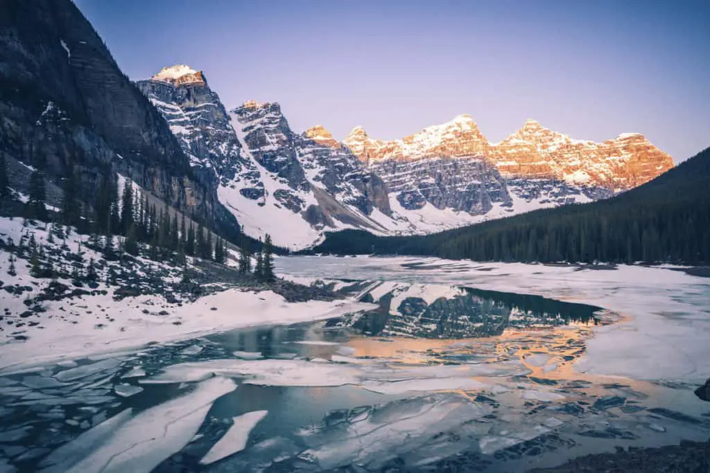 A frozen Moraine Lake at sunset under a clear winter sky with the surrounding Rocky Mountains covered in snow