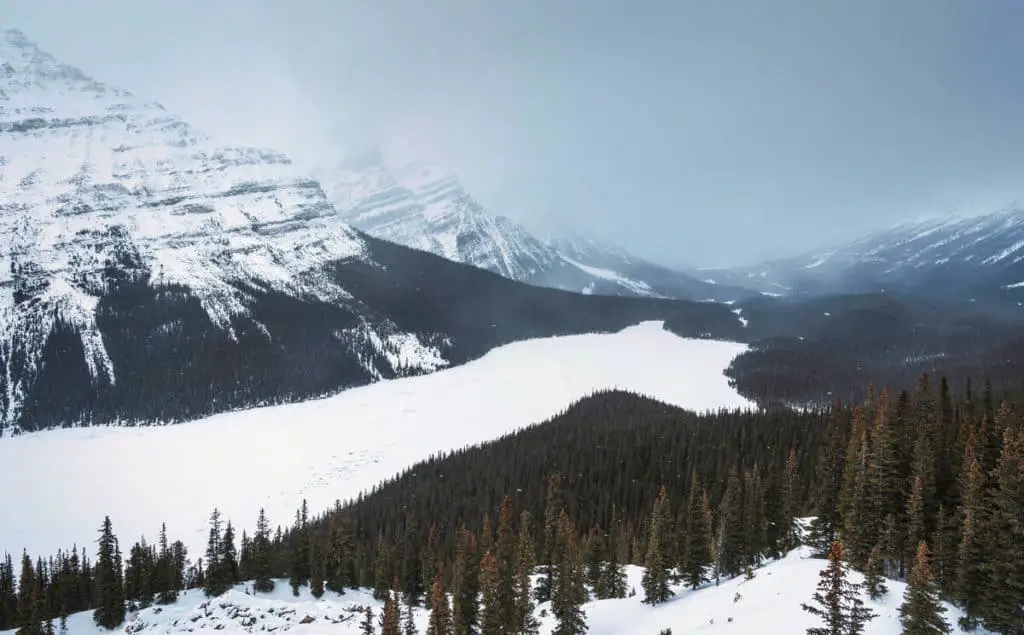 A frozen and snowy Peyto Lake under a grey, ominous sky with snow clouds
