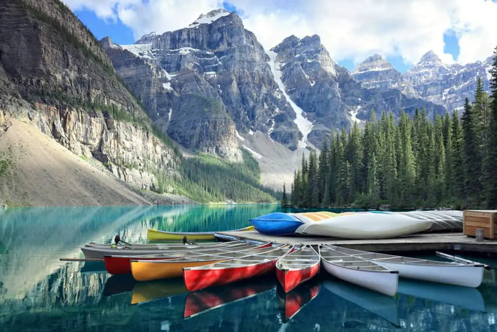 Colorful canoes lie in the water near the jetty at Moraine Lake with the Valley of the Ten Peaks towering high above in the background