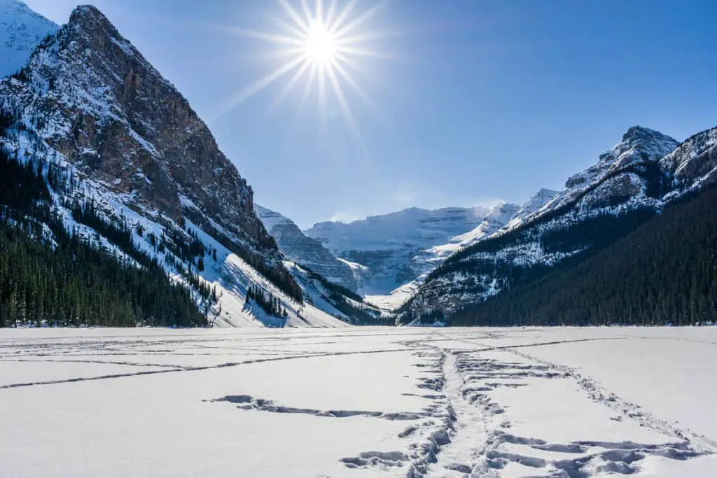 A bright sun shines upon a frozen and snow-covered Lake Louise in Banff National Park
