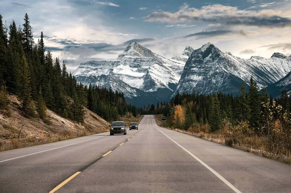 A car driving on the Icefields Parkway with high, snow-covered mountains in the background in Banff National Park