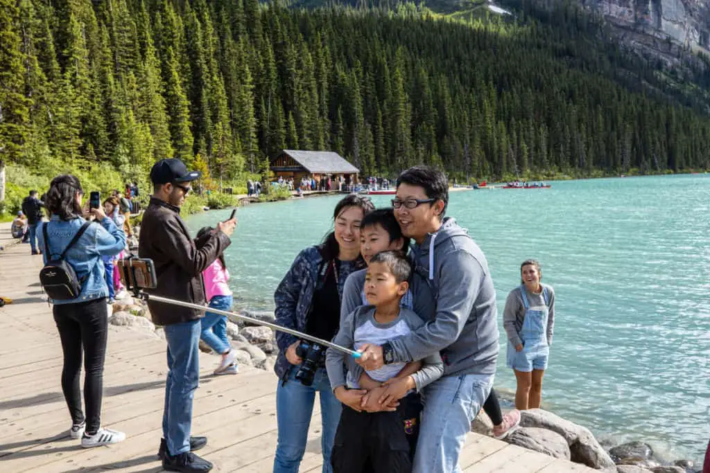 An Chinese family of four is standing at the Lake Louise lakeshore taking a selfie utilizing a selfie stick