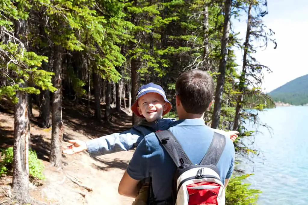 A father holding his son while hiking along a lake in Banff National Park