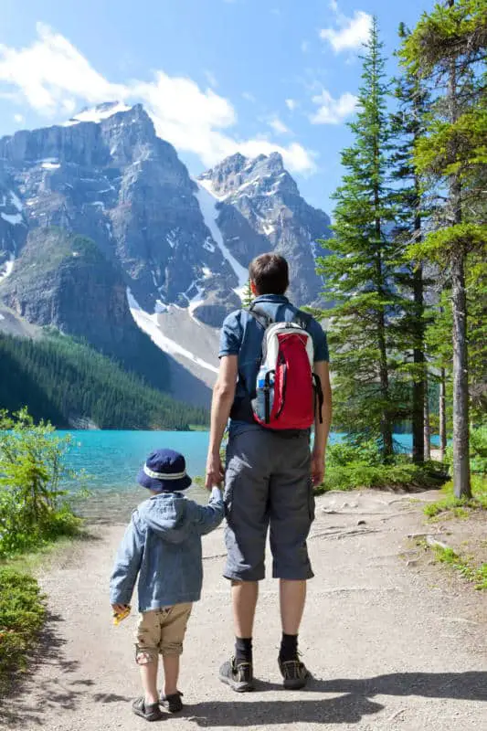 A father is holding the hand of his todler son while hiking along the Moraine Lake lakeshore