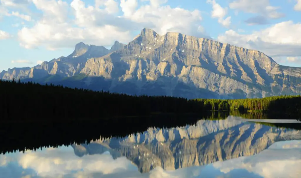 Mountains reflect in the still waters of Johnson Lake during sunrise in Banff National Park