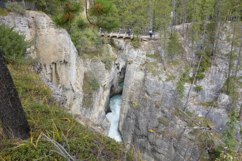 A wooden bridge crosses the deep Mistaya Canyon while water rushes through it