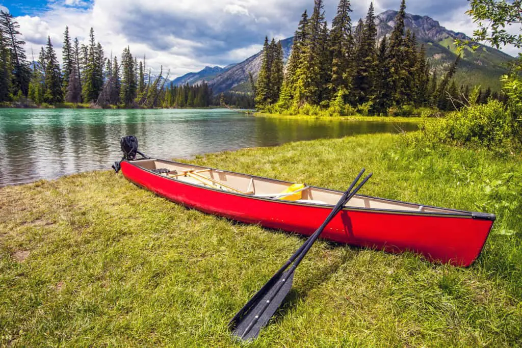 A big, red canoe with a black paddle resting on the shore of the Bow River