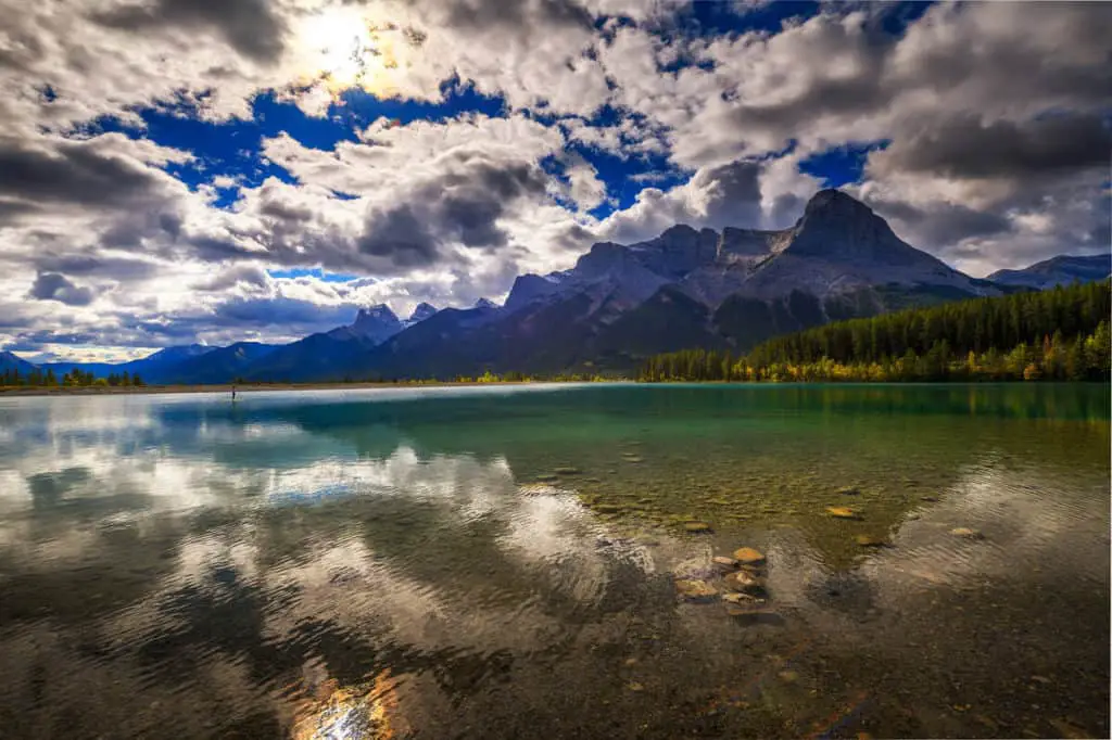 A man stands on his SUP on the Rundle Forebay Reservoir in Canmore, with Rundle Mountain in the background