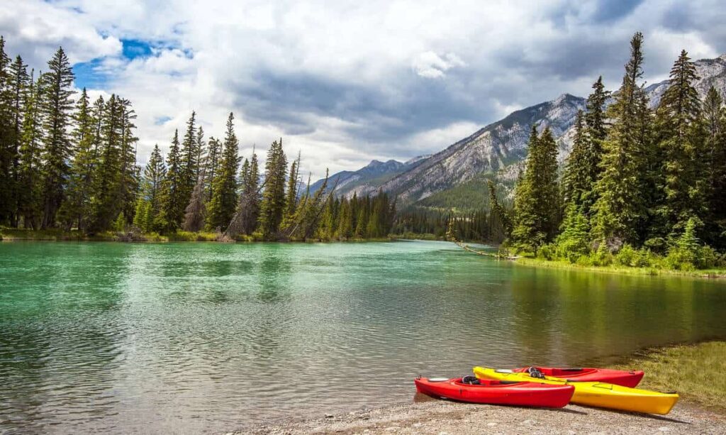 Two red canoes and one yellow one resting on the shore of the Bow River near the town of Banff