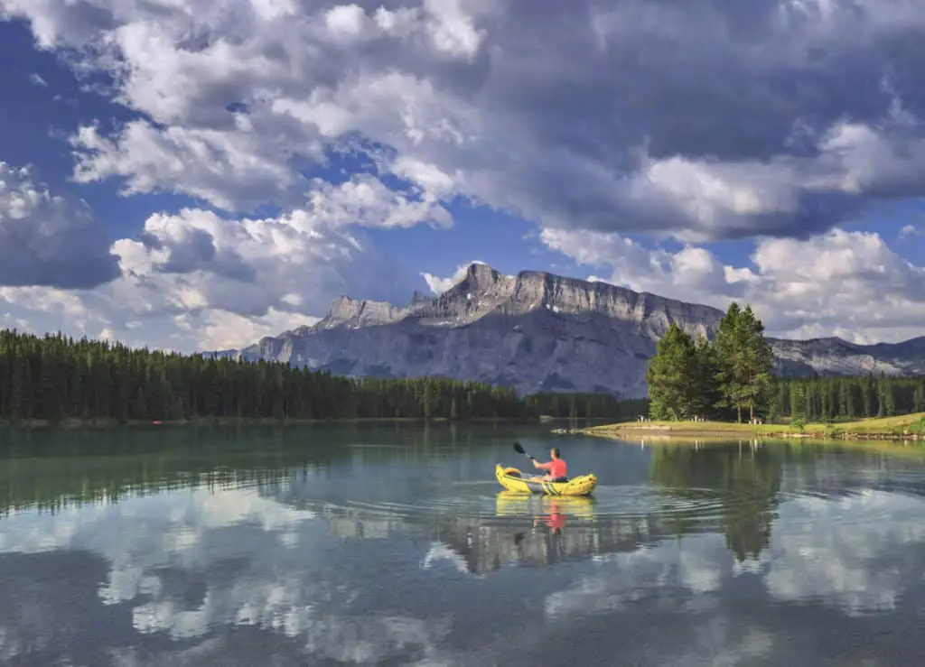 A man canoeing on Two Jack Lake during a cloudy day with Mount Rundle in the background