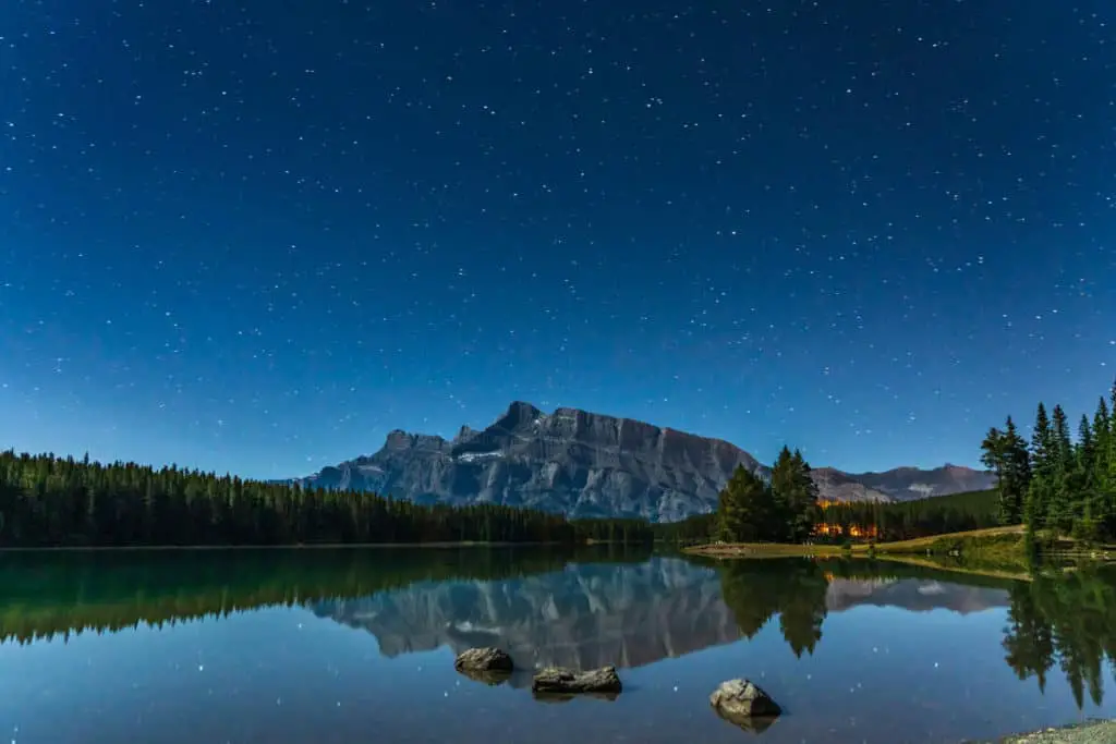 A starry night over the tranquil water of Two Jack Lake in Banff National Park with Mount Rundle in the background
