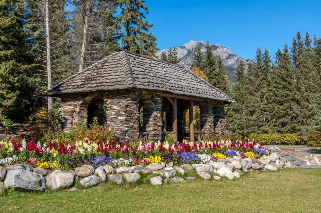 The iconic Cambrian Pavilion surround by colorful flowers and pine trees at the Cascades of Time Garden in Banff