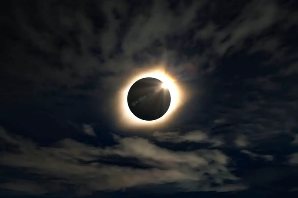 A full solar eclipse in a cloudy sky, creating shades of dark blue colors