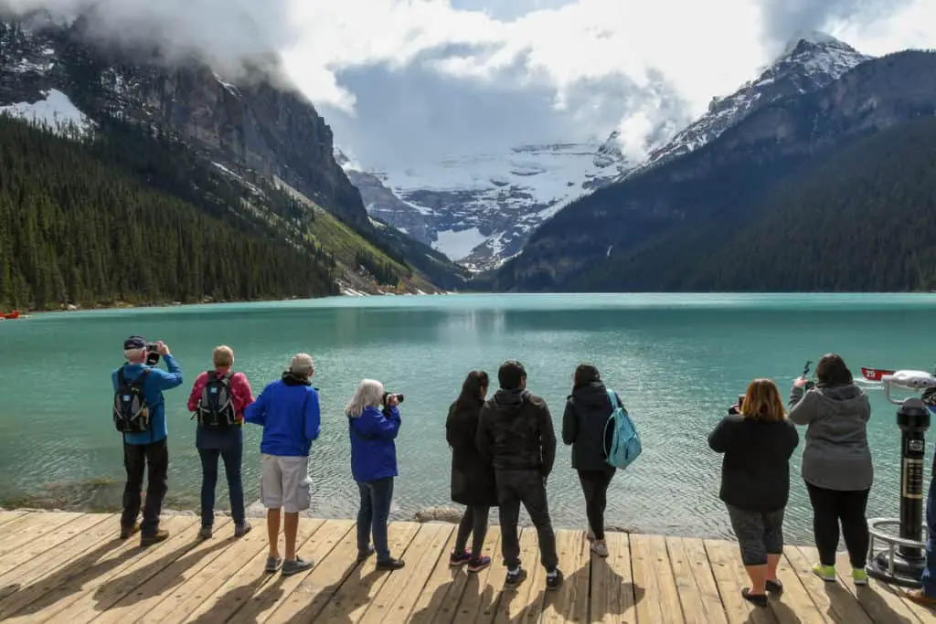 Tourists at the Lake Louise lakeshore seen on their back, admiring the lake's beauty