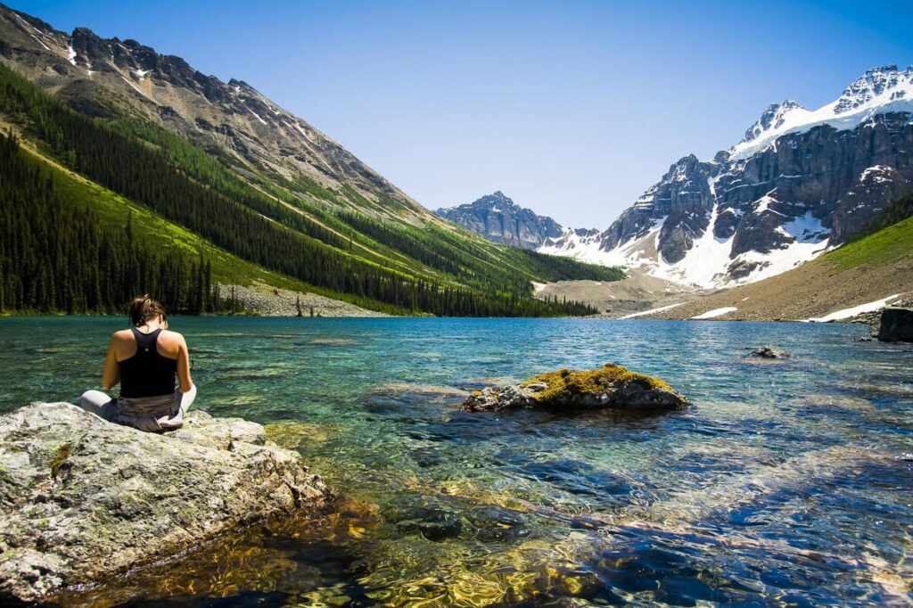 A woman is enjoying the scenery with snow-capped mountains surrounding Consolation Lakes in Banff National Park