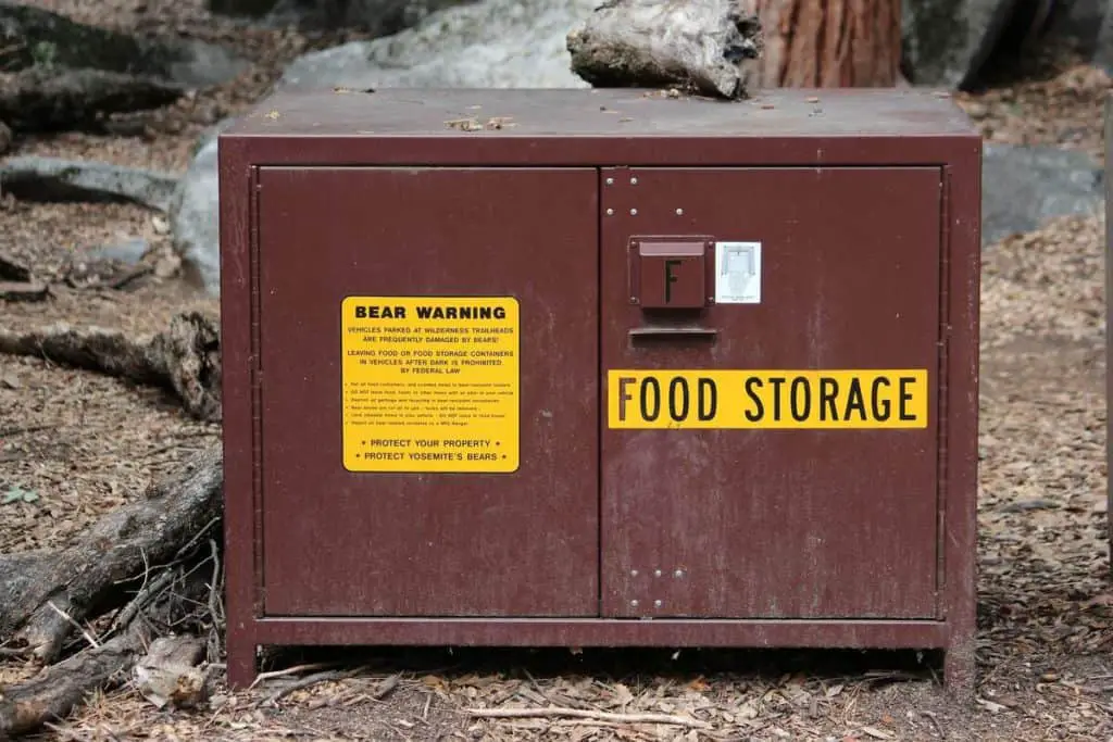 A brown bear proof food-storage unit at a campground adorned with a sticker mentioning "bear warning"