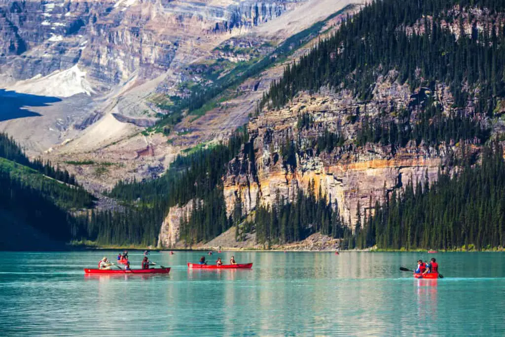 People in red canoes canoeing on the famous Lake Louise in Banff National Park with Mount Victoria in the background
