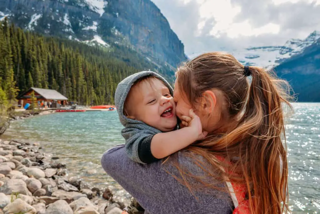 A mother cuddles her toddler she's holding in her arms while standing at the lakeshore of Lake Louise in Banff, Alberta