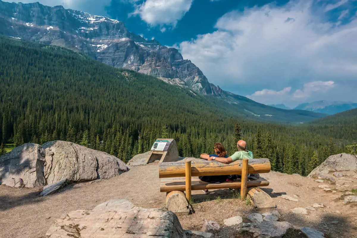 A senior couple sitting at a wooden bench overlooking a valley near Moraine Lake in Banff National Park