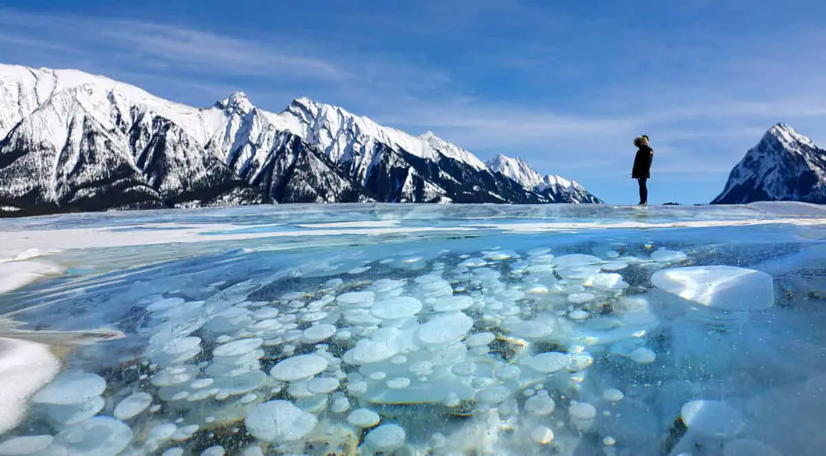Woman standing on frozen Abraham Lake in Alberta with methane bubbles visible in the foreground