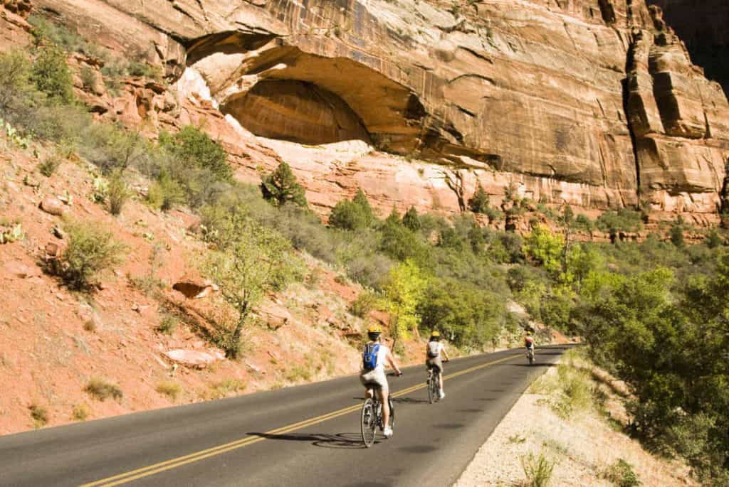 Three people cycling through Zion National Park with a giant rock rising to the left